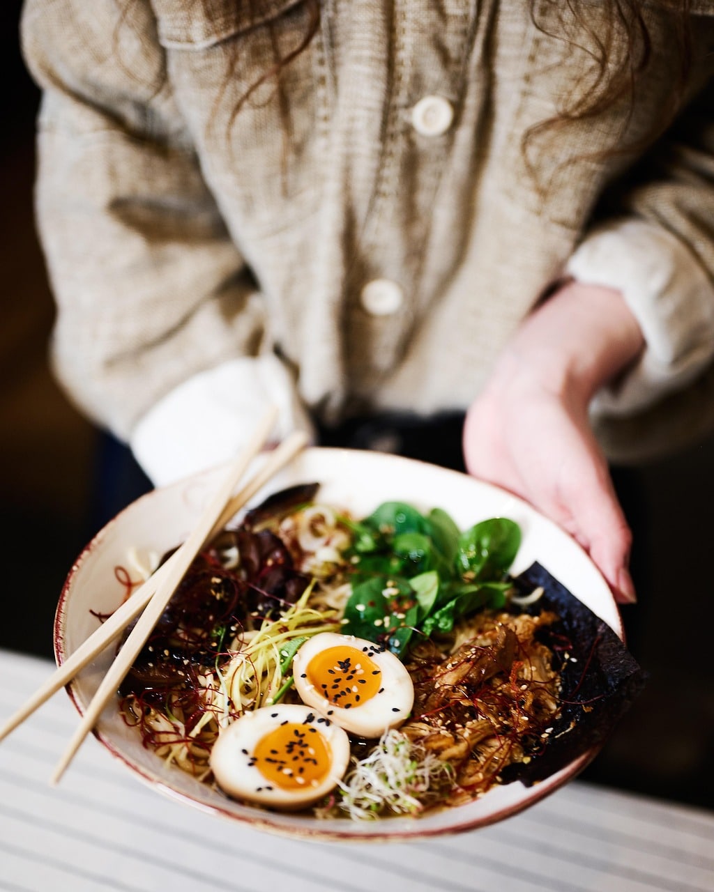 Person holding a bowl of ramen with eggs